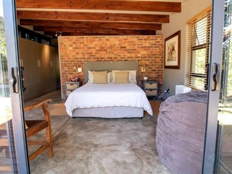 Spacious bedroom featuring exposed brick feature wall, polished concrete flooring, and exposed timber ceiling beams with large sliding glass doors.