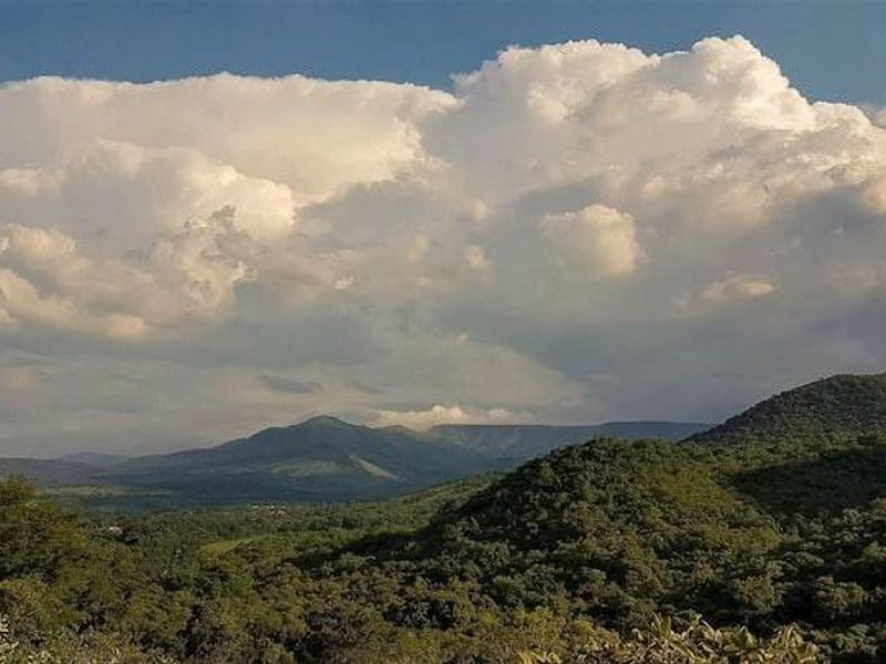A scenic view of rolling green hills and mountains under a dramatic cloudy sky.