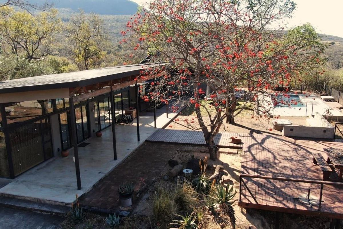 Aerial view of a modern residence featuring a spacious covered patio, expansive wooden decking, and a swimming pool set against a natural landscape.