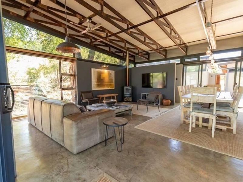 Spacious open-plan living and dining area featuring exposed timber roof trusses, polished concrete floors, and a built-in wood-burning fireplace.