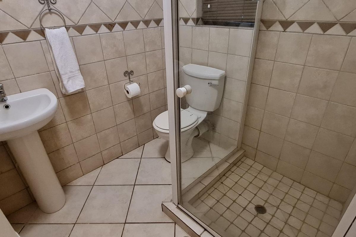 A functional bathroom featuring a pedestal basin, toilet, and a glass-enclosed shower with neutral ceramic tiling throughout.
