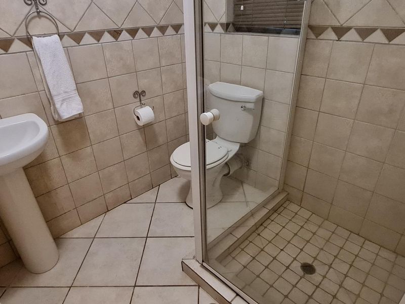 A functional bathroom featuring a pedestal basin, toilet, and a glass-enclosed shower with neutral ceramic tiling throughout.