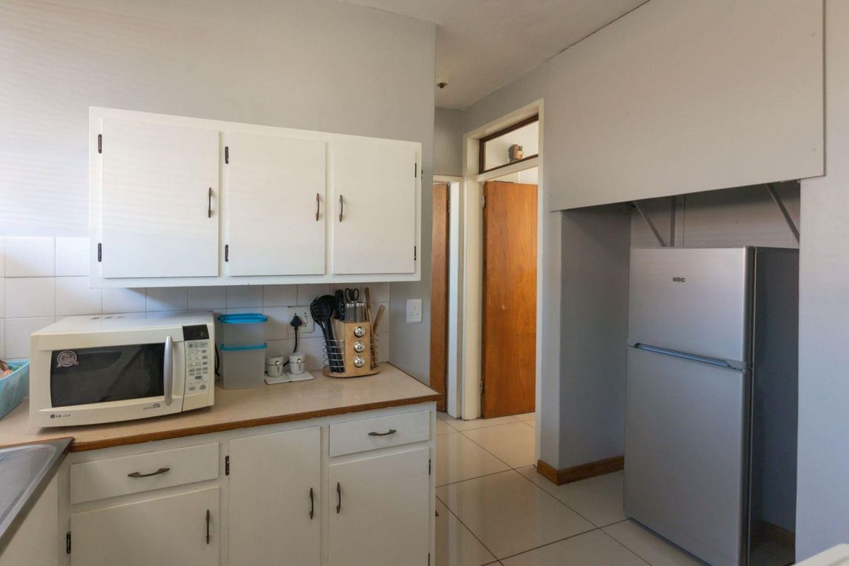 A functional kitchen featuring white cabinetry, tiled flooring, and a dedicated alcove for a refrigerator, leading into a hallway with wooden doors.