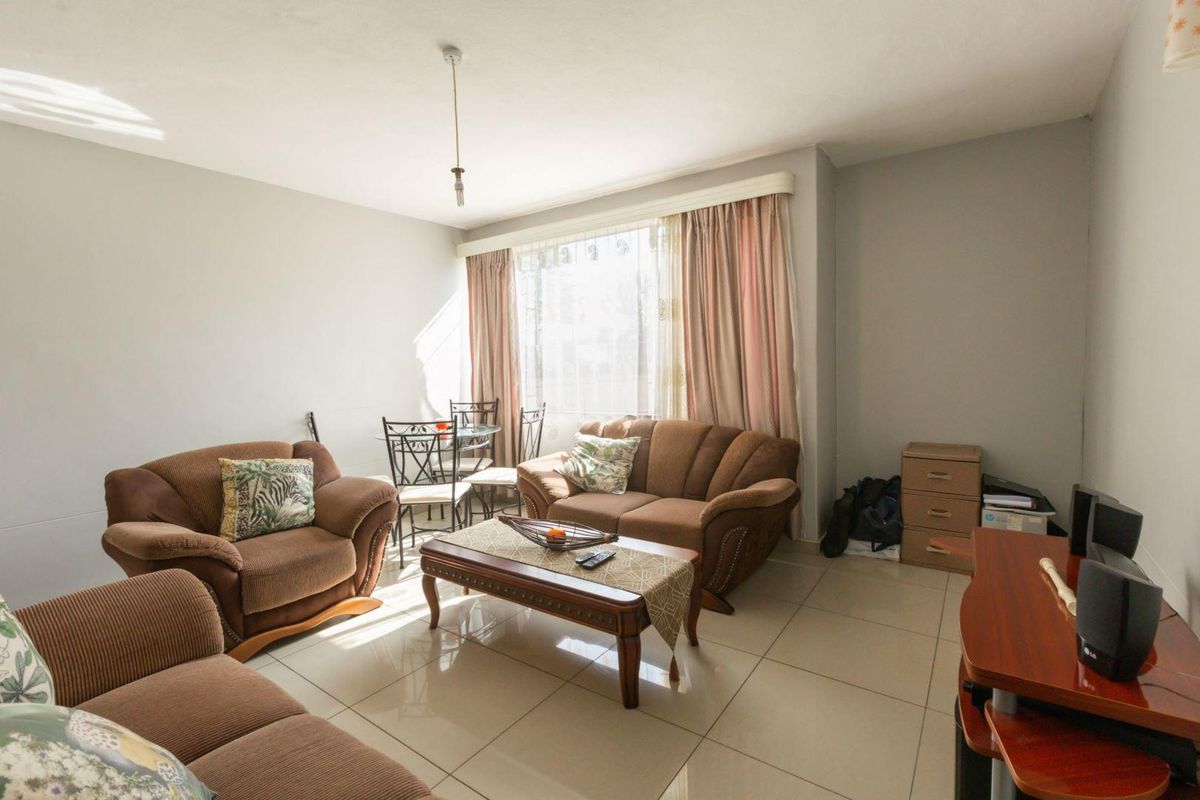 A bright living room featuring large windows, neutral tiled flooring, and a functional layout suitable for comfortable seating and dining arrangements.
