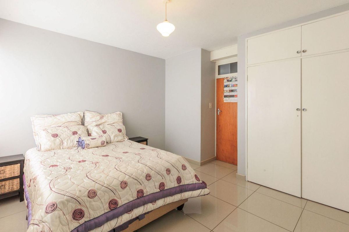 A functional bedroom featuring neutral tiled flooring, built-in white cabinetry, and a standard wooden door.