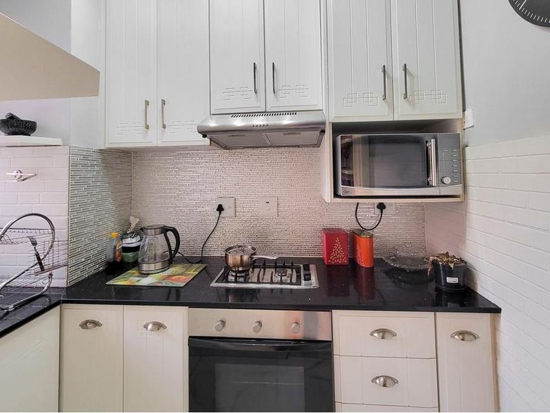 A functional kitchen featuring white cabinetry, granite countertops, a mosaic tile backsplash, and integrated appliances including a gas hob, oven, and microwave.