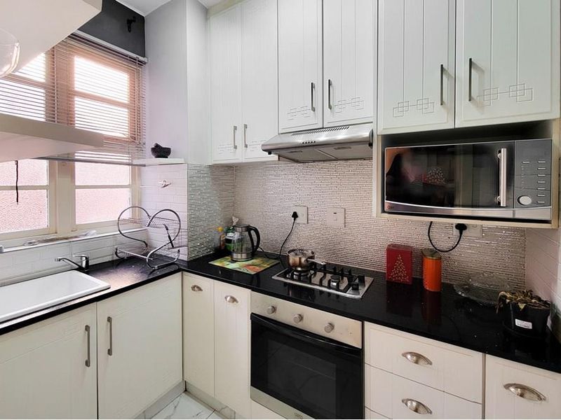 A well-maintained kitchen featuring white cabinetry, black granite countertops, a gas hob, built-in oven, and a modern tiled backsplash.