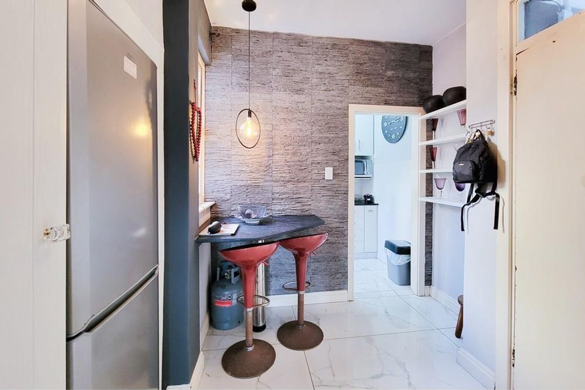 A compact kitchen area featuring a stone-clad feature wall, built-in breakfast bar, modern pendant lighting, and polished tiled flooring, leading into a secondary kitchen space.