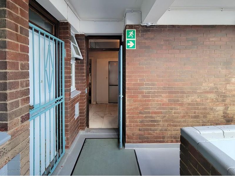 An exterior entrance area featuring exposed brick walls, a security gate, and tiled flooring, providing access to the interior of the property.