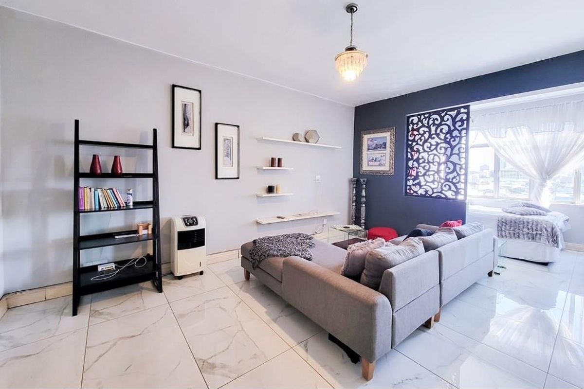 Open-plan living area featuring polished marble-look floor tiles, decorative wall shelving, and a stylish laser-cut room divider separating the living and sleeping zones.