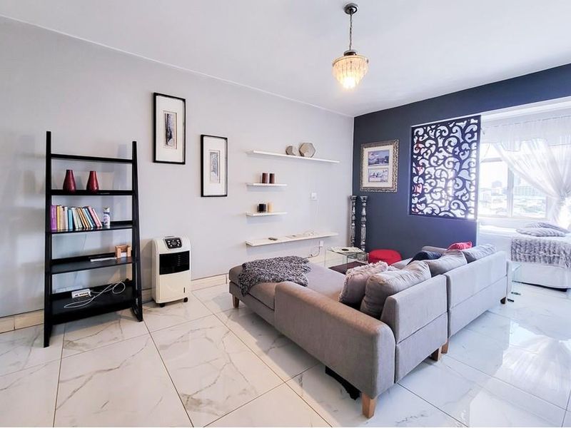 Open-plan living area featuring polished marble-look floor tiles, decorative wall shelving, and a stylish laser-cut room divider separating the living and sleeping zones.