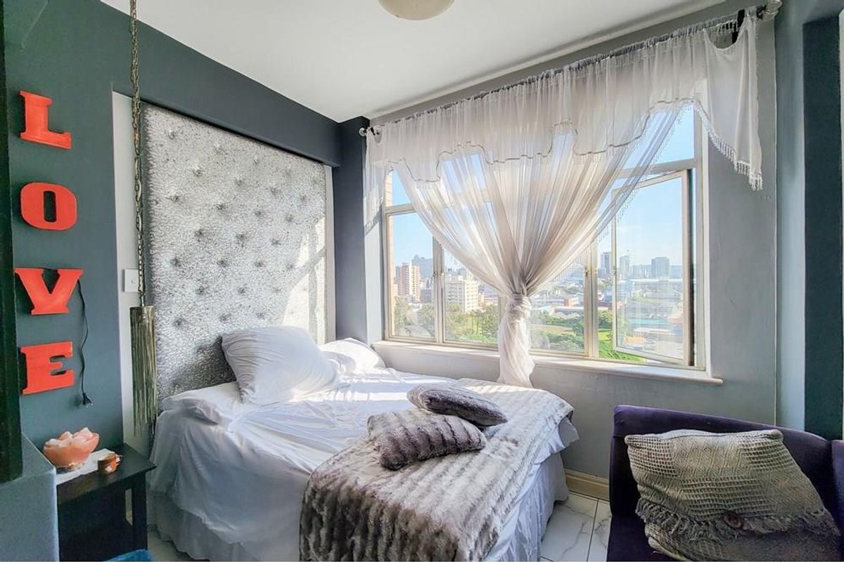 A bedroom featuring a large window with city views, tiled flooring, and a decorative built-in headboard.