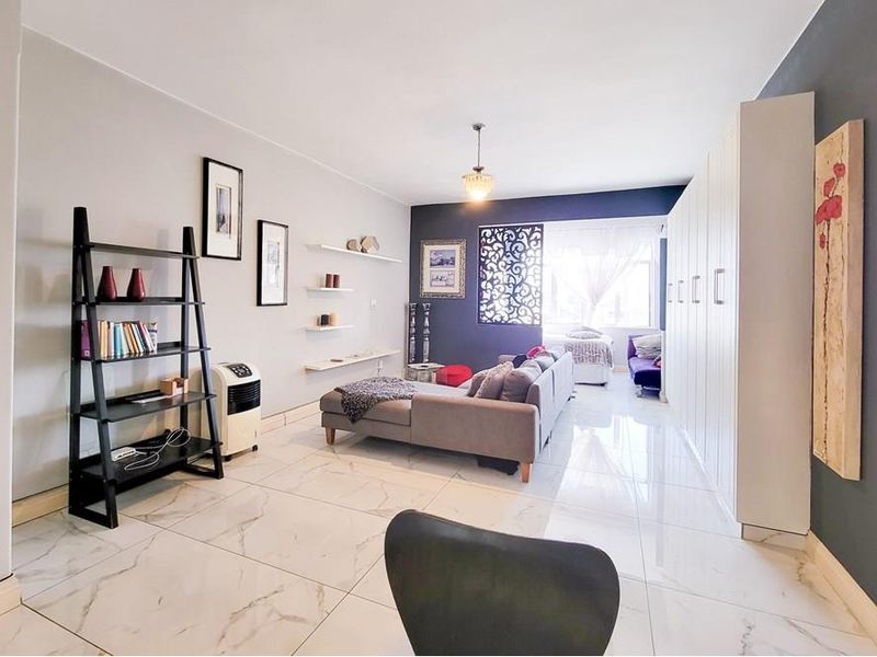 Spacious living area featuring polished marble-look floor tiles, extensive built-in storage cabinetry, and a decorative feature wall screen.