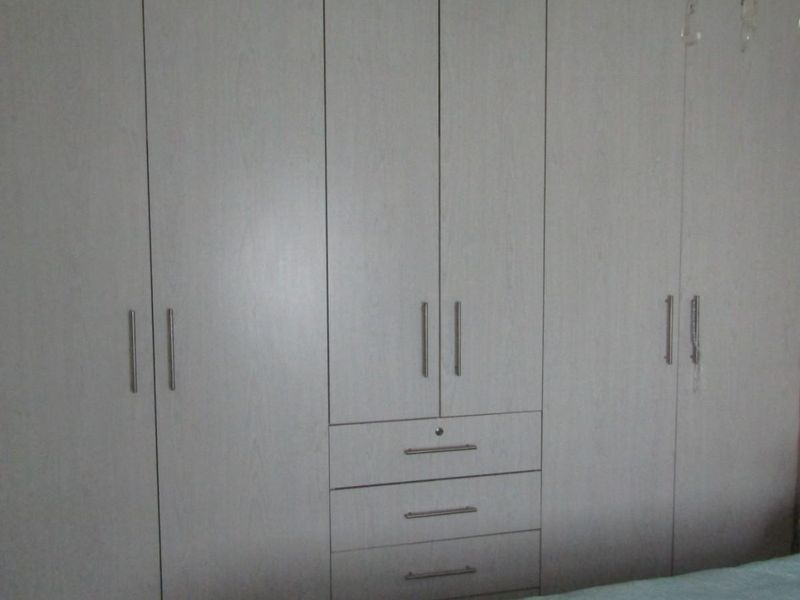 A bedroom featuring a large, light-toned built-in wardrobe with integrated storage drawers and modern metal handles.