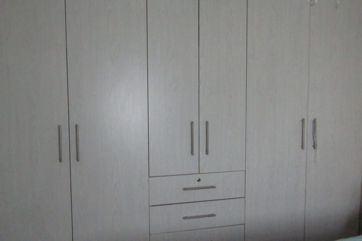 A bedroom featuring a large, light-toned built-in wardrobe with integrated storage drawers and modern metal handles.
