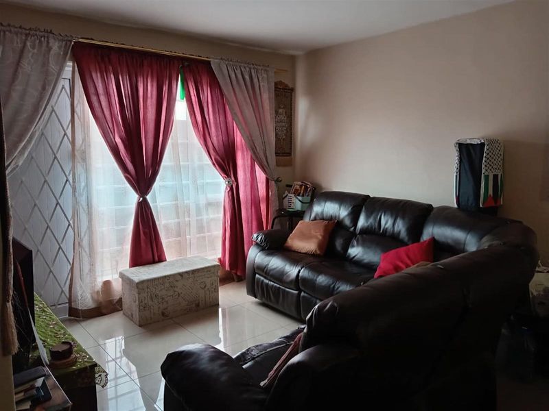 A living room featuring tiled flooring and a sliding glass door with a security gate, providing access to the exterior.