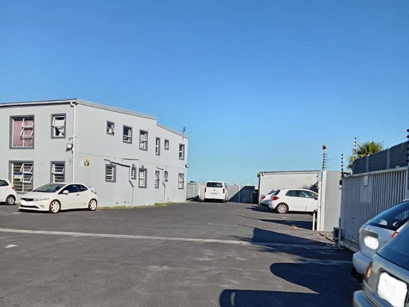 Exterior view of the apartment complex showing the paved parking area, perimeter security fencing, and building facade.