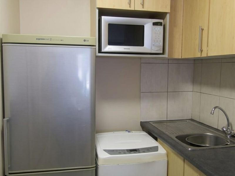 Compact scullery area featuring light wood-finish cabinetry, laminate countertops, a stainless steel sink, and dedicated space for laundry and kitchen appliances.