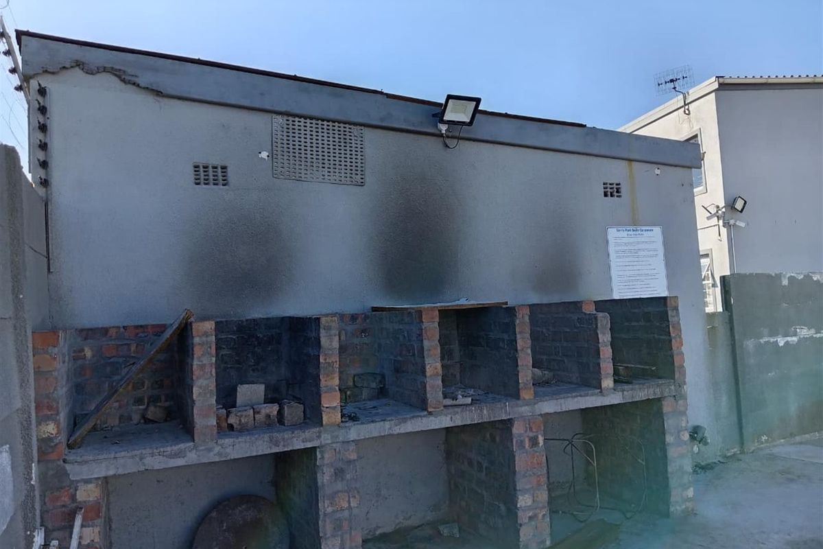 Outdoor communal braai area featuring multiple brick-built cooking stations with significant soot staining and visible wear to the surrounding wall structure.