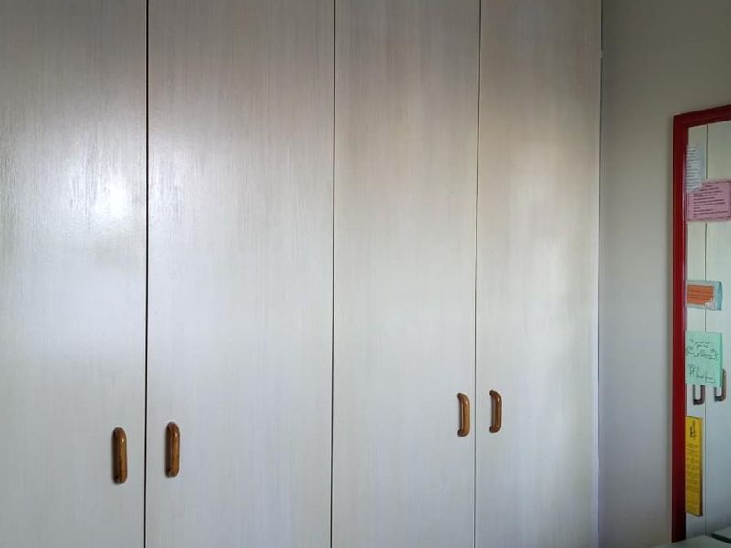 A bedroom featuring floor-to-ceiling built-in cupboards with light wood-grain finish and simple hardware.