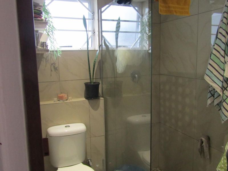 Compact bathroom featuring a glass-enclosed shower with pebble flooring, tiled walls, and a standard toilet.