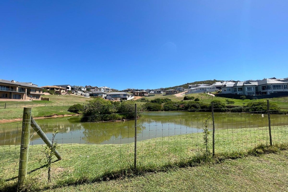 A scenic view of a residential estate featuring a central pond, landscaped green areas, and surrounding modern homes under a clear blue sky.