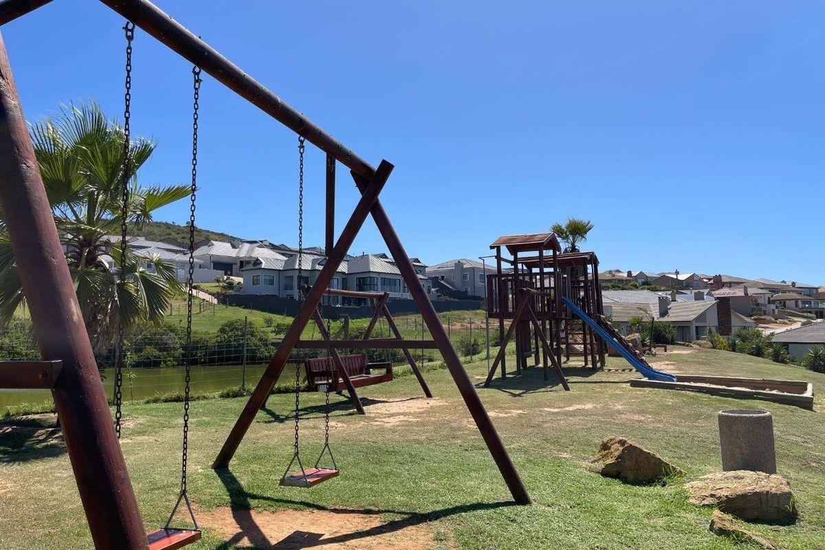 A well-maintained residential garden area featuring a wooden playground set, swing structure, and landscaped lawn within a secure estate setting.