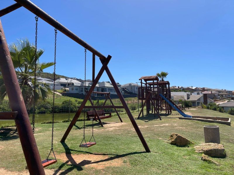 A well-maintained residential garden area featuring a wooden playground set, swing structure, and landscaped lawn within a secure estate setting.