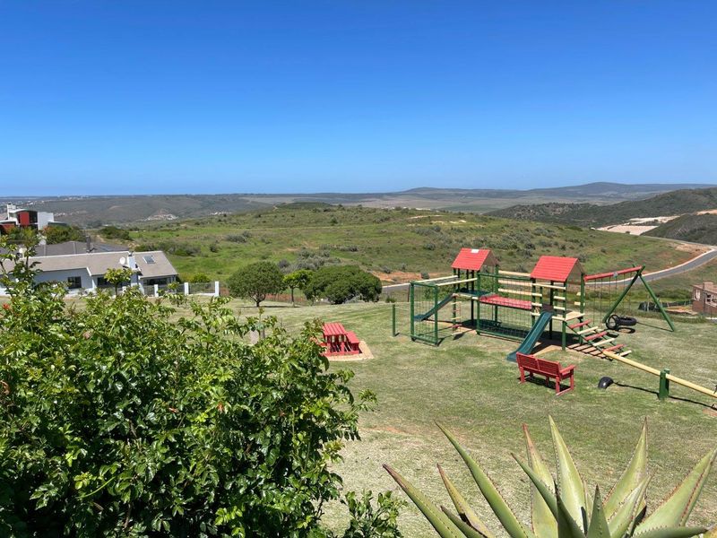 A scenic elevated view overlooking a landscaped garden area with playground equipment and expansive rolling hills in the background.