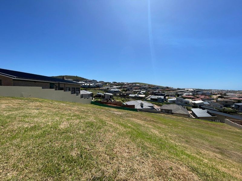 A wide-angle view of a sloped residential plot overlooking a coastal neighborhood and surrounding landscape.