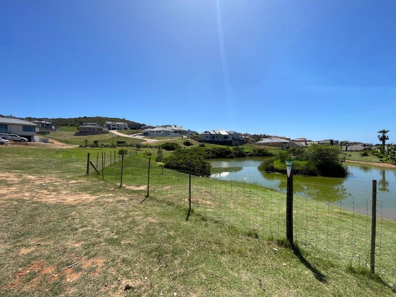 A scenic view of a natural pond and surrounding residential landscape, featuring wire mesh perimeter fencing and open green space.