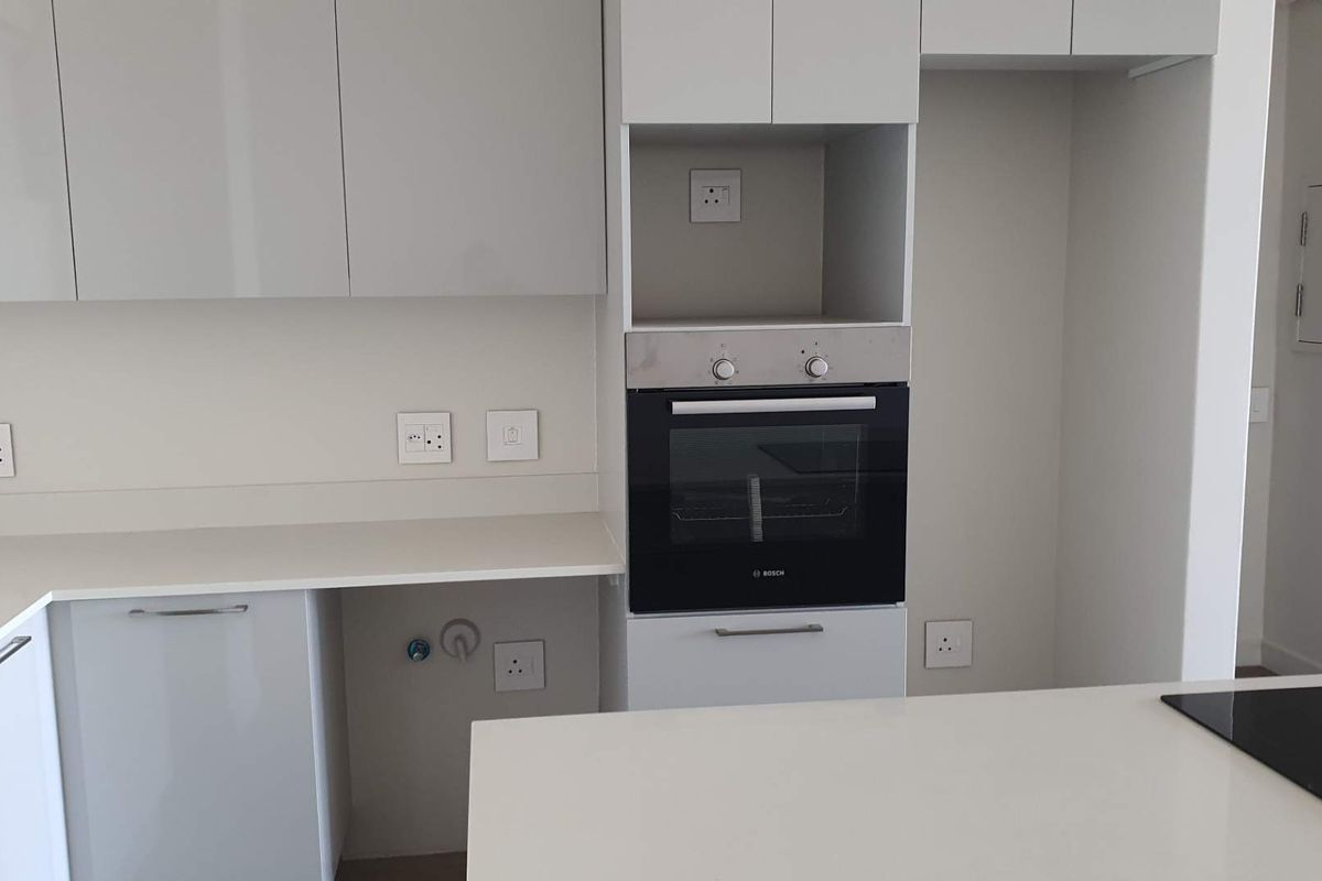 Modern kitchen featuring sleek white cabinetry, integrated oven, and stone countertops with ample workspace and clean, minimalist finishes.