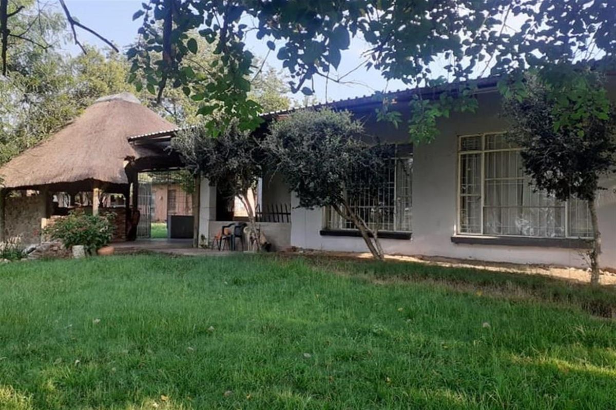 A view of the rear exterior of the property featuring a lawn, a thatched-roof outdoor area, and large windows with security bars.