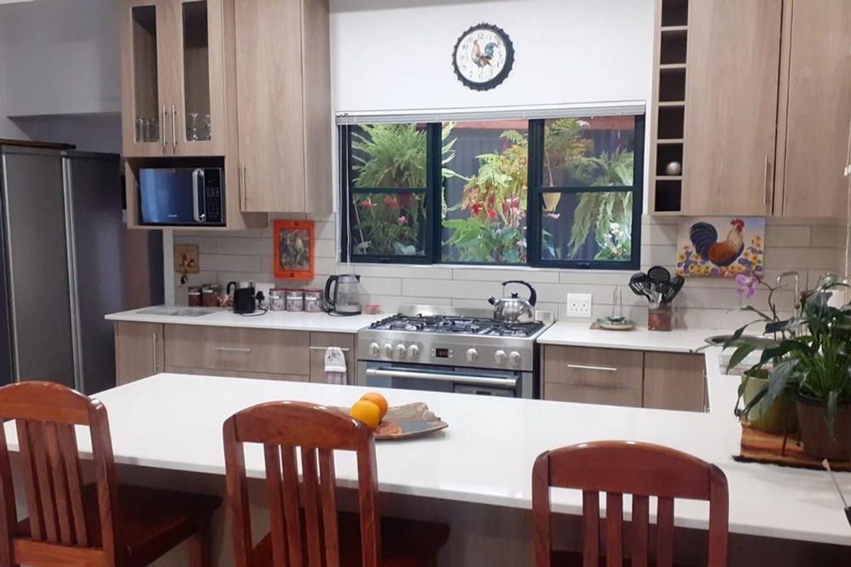 A well-maintained kitchen featuring light wood cabinetry, a gas stove, a breakfast bar with stone countertops, and a window overlooking a lush garden.