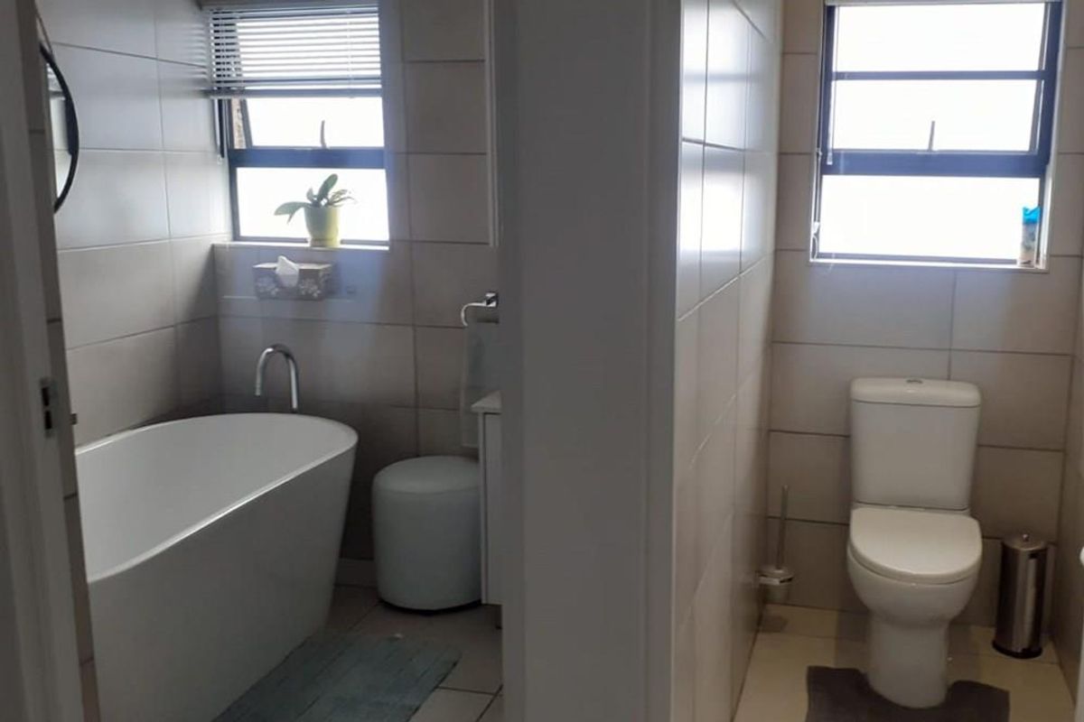 A modern bathroom featuring a freestanding bathtub and a separate enclosed toilet area with neutral wall tiling and natural light.