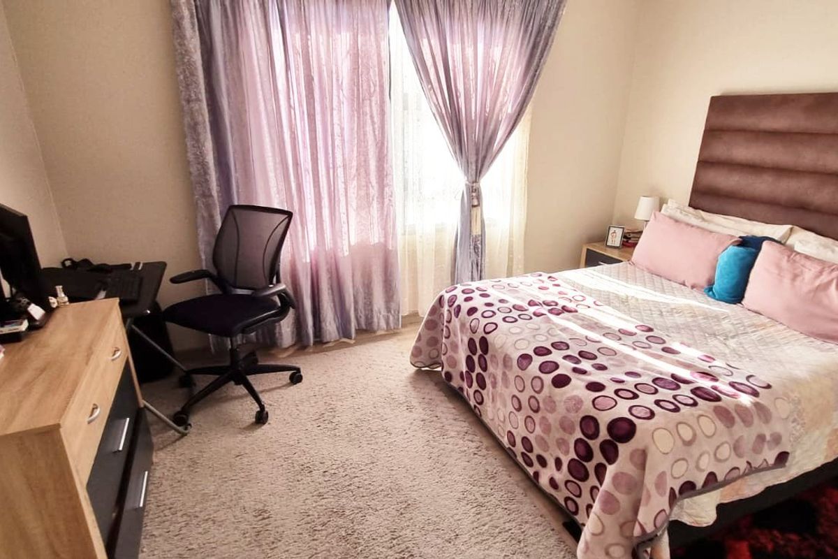 A well-lit bedroom featuring neutral wall finishes, carpeted flooring, and a large window with curtain treatments.
