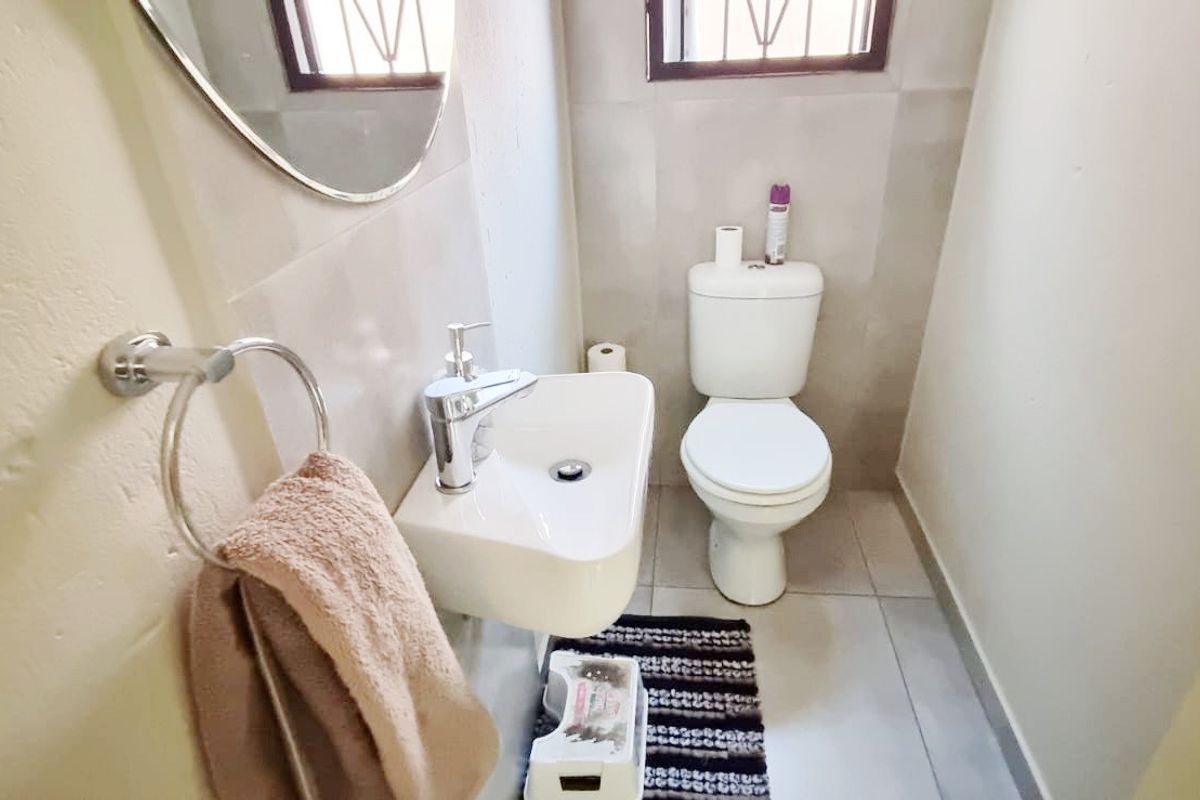 A compact guest bathroom featuring a wall-mounted basin, a standard toilet, and tiled flooring with neutral wall finishes.