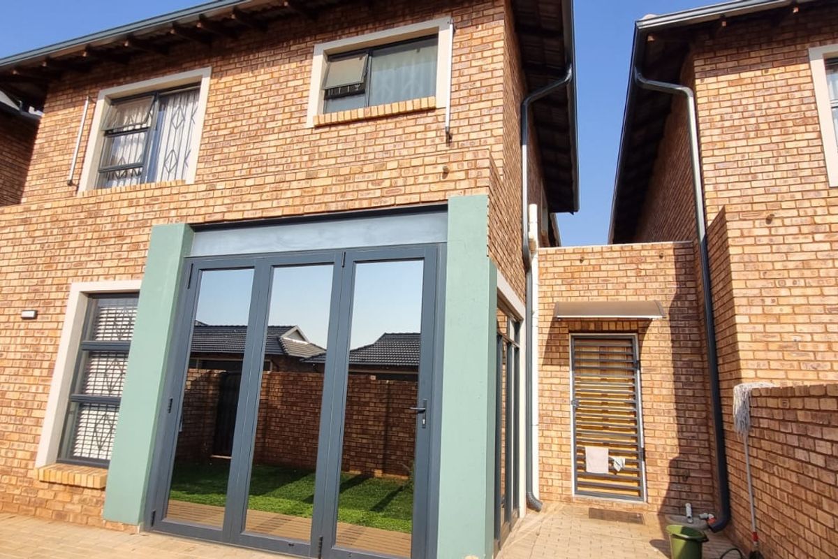 Rear view of a double-story brick townhouse featuring large glass stacker doors, paved patio area, and a secure side entrance.