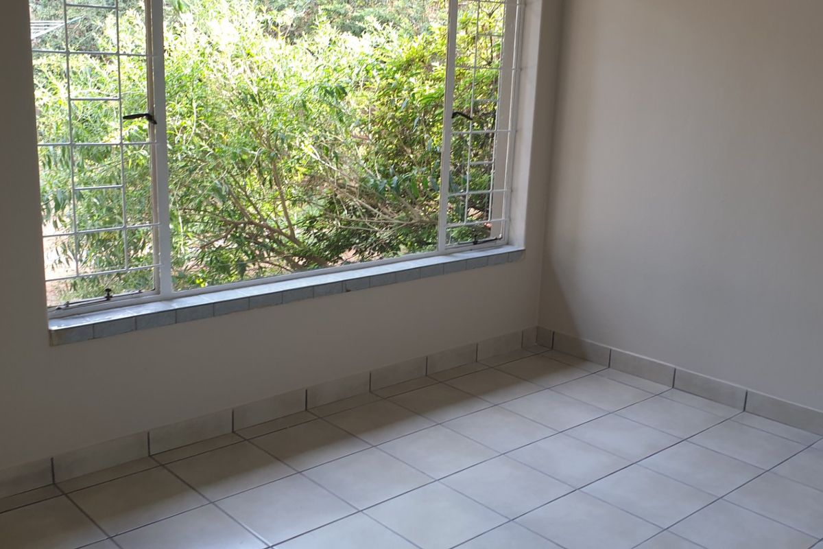 An empty bedroom featuring neutral tiled flooring and large windows with security bars, offering a bright and clean space ready for personalization.