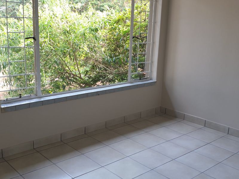 An empty bedroom featuring neutral tiled flooring and large windows with security bars, offering a bright and clean space ready for personalization.