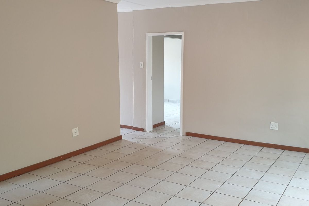 An empty living area featuring neutral painted walls, ceramic floor tiles, and a clear transition to an adjacent room.