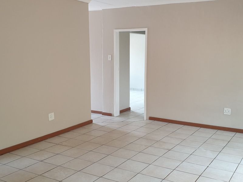 An empty living area featuring neutral painted walls, ceramic floor tiles, and a clear transition to an adjacent room.