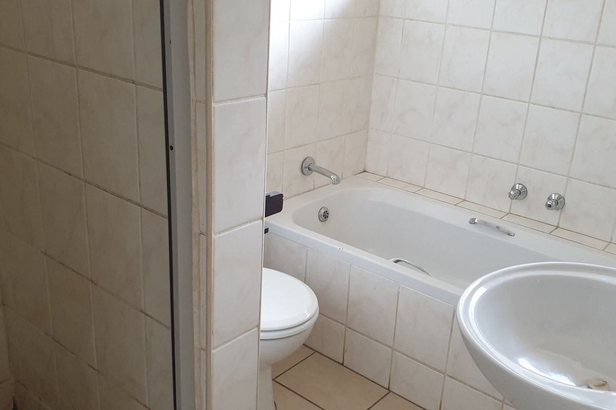 A dated bathroom featuring a standard bathtub, pedestal basin, and neutral ceramic wall and floor tiles.