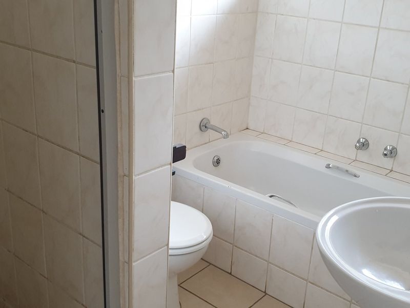 A dated bathroom featuring a standard bathtub, pedestal basin, and neutral ceramic wall and floor tiles.