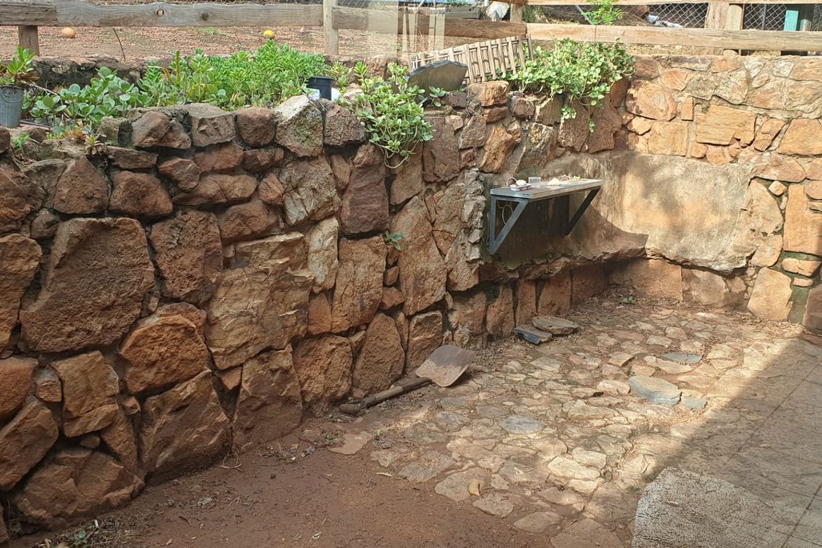 A rustic outdoor rear courtyard area featuring natural stone retaining walls, stone paving, and a wall-mounted metal shelf.