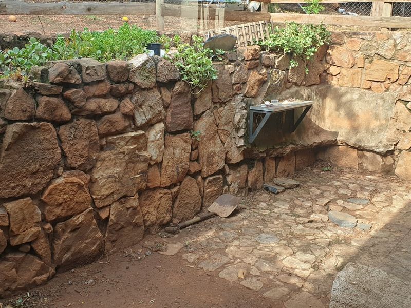 A rustic outdoor rear courtyard area featuring natural stone retaining walls, stone paving, and a wall-mounted metal shelf.