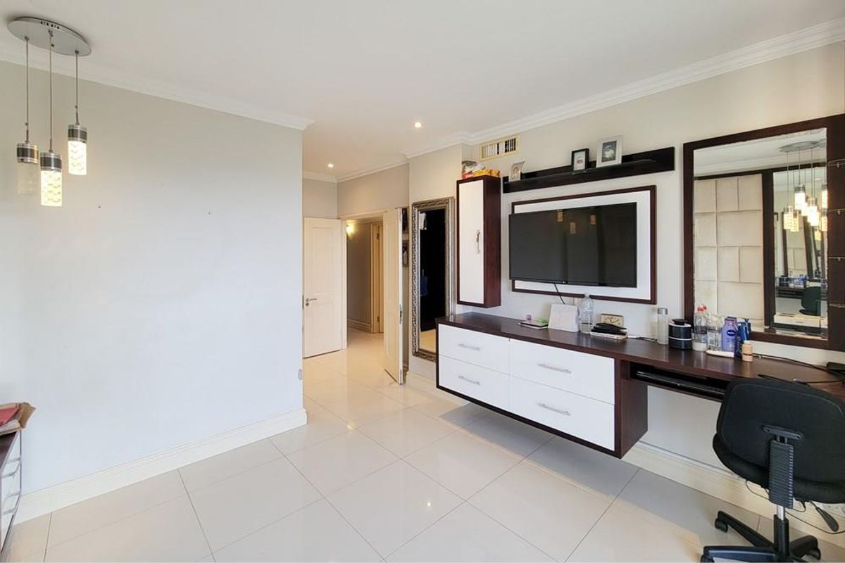 A well-maintained living area featuring polished floor tiles, recessed ceiling lighting, and a custom built-in wall unit with integrated storage and desk space.