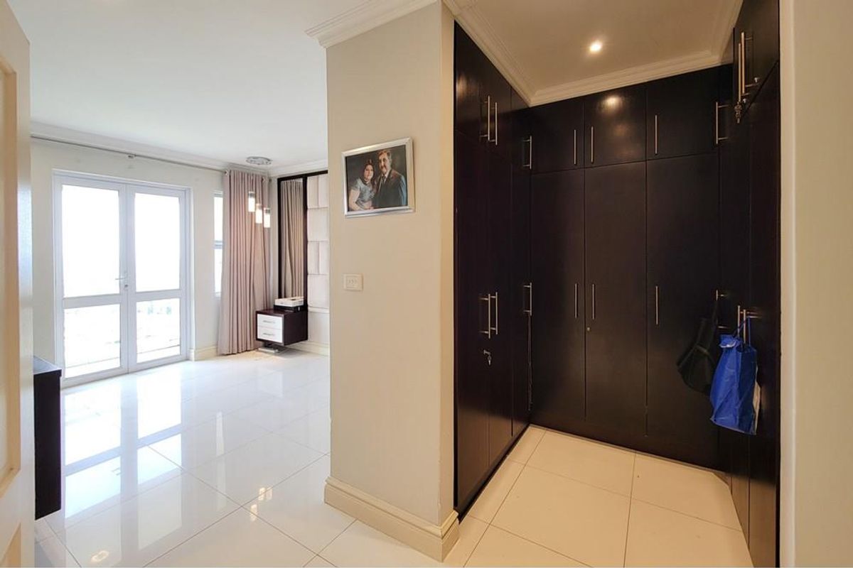 A bright bedroom featuring polished tile flooring, recessed ceiling lighting, and extensive dark wood built-in cabinetry providing ample storage space.