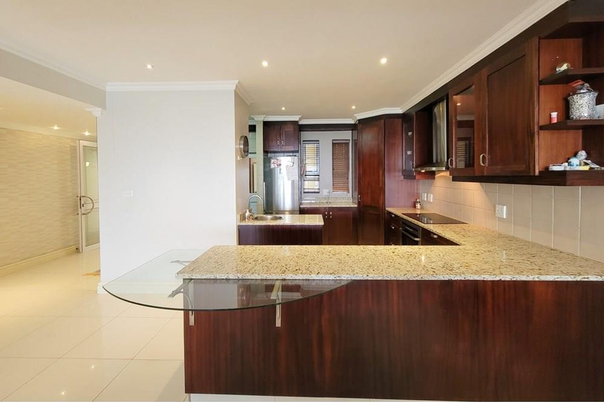 A well-maintained kitchen featuring dark wood cabinetry, granite countertops, a breakfast bar, and integrated appliances, seamlessly flowing into the adjacent living area.