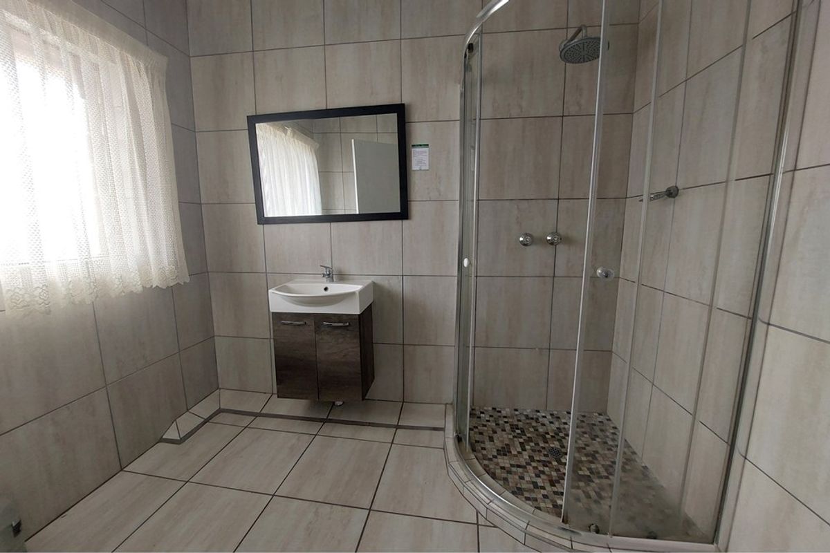 A modern bathroom featuring a curved glass shower enclosure, tiled walls and flooring, and a wall-mounted vanity with a basin.